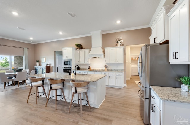 kitchen featuring a breakfast bar area, visible vents, appliances with stainless steel finishes, premium range hood, and white cabinets