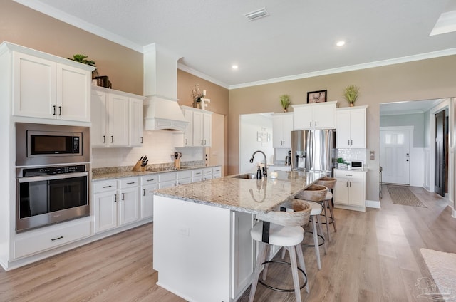 kitchen with white cabinets, stainless steel appliances, ornamental molding, and a sink