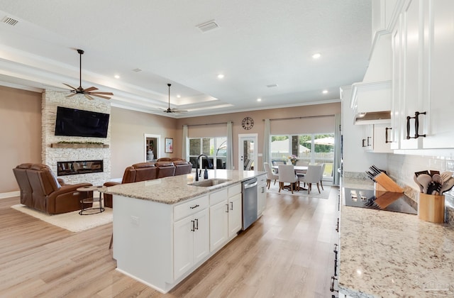 kitchen featuring visible vents, a ceiling fan, a stone fireplace, white cabinets, and a sink