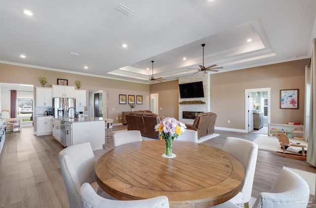 dining area with ornamental molding, a fireplace, baseboards, a tray ceiling, and a ceiling fan