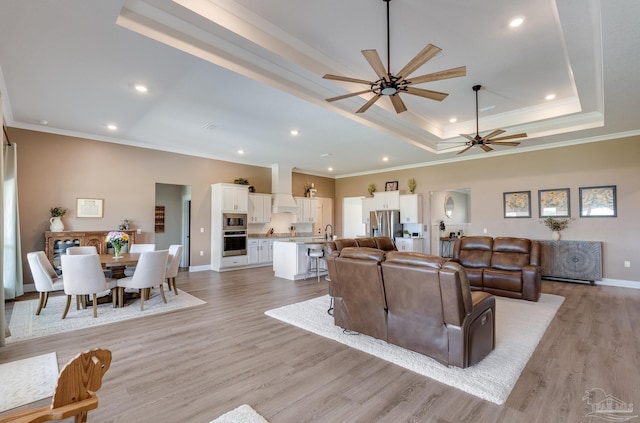 living room with a raised ceiling, ornamental molding, a ceiling fan, and light wood-style flooring