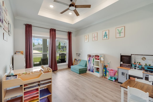 playroom featuring a ceiling fan, ornamental molding, light wood-style flooring, and a raised ceiling