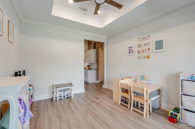 game room featuring a raised ceiling, light wood-style flooring, a ceiling fan, visible vents, and ornamental molding