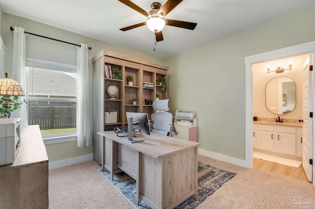 office featuring a sink, baseboards, light carpet, and a ceiling fan