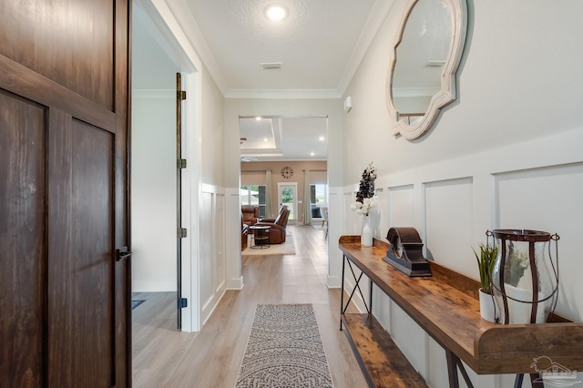 corridor with wainscoting, light wood-style floors, a decorative wall, visible vents, and ornamental molding