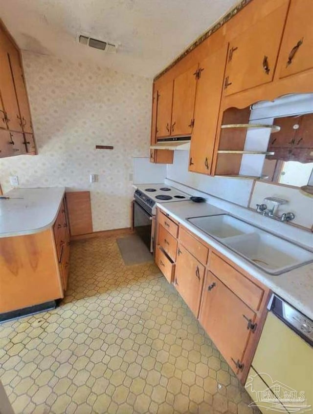 kitchen featuring a sink, wallpapered walls, white appliances, light countertops, and light floors