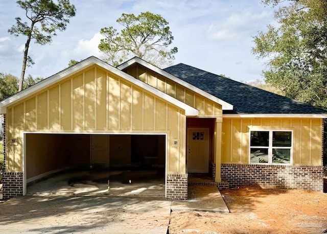 view of front facade with driveway, roof with shingles, board and batten siding, an attached garage, and brick siding