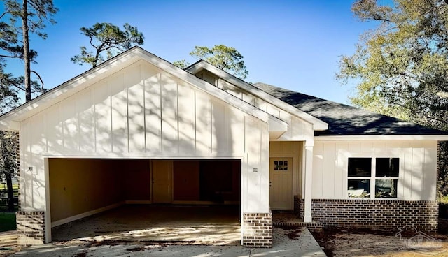 view of front facade featuring brick siding, board and batten siding, a shingled roof, a garage, and driveway