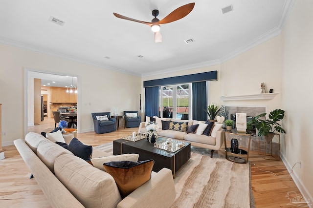 living room featuring a tile fireplace, light hardwood / wood-style floors, ornamental molding, and ceiling fan