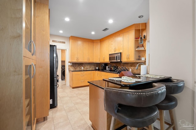 kitchen featuring light brown cabinets, black fridge, decorative light fixtures, backsplash, and a breakfast bar area