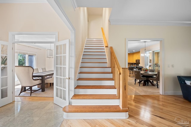 stairs featuring an inviting chandelier, wood-type flooring, and ornamental molding