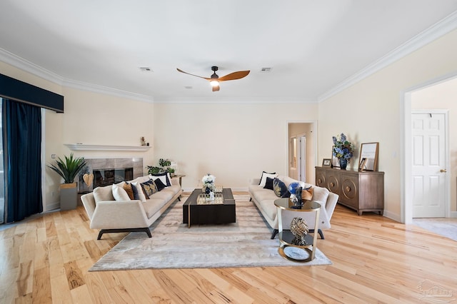 living room with light wood-type flooring, a tiled fireplace, ceiling fan, and crown molding