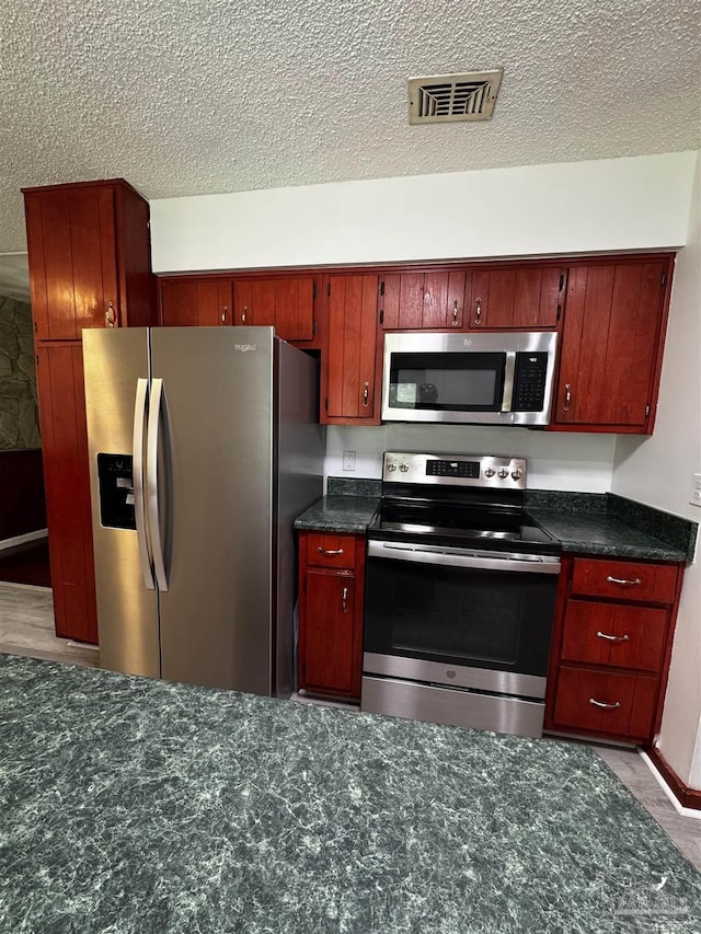 kitchen with dark stone countertops, visible vents, a textured ceiling, and appliances with stainless steel finishes