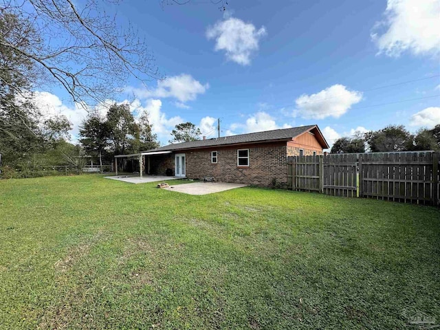 rear view of house featuring brick siding, fence, a lawn, a carport, and a patio