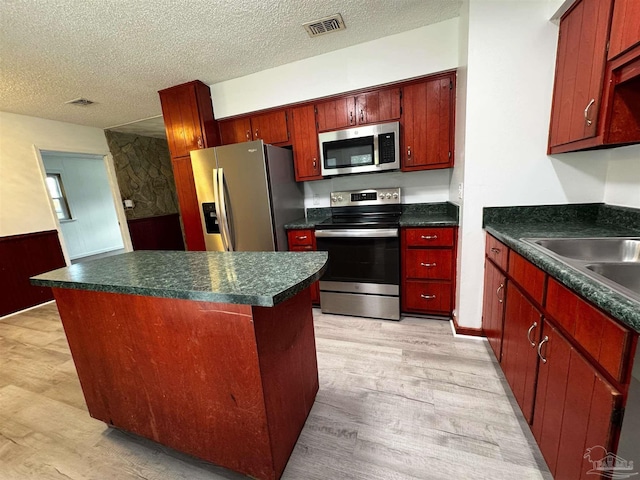 kitchen with light wood-type flooring, a sink, a kitchen island, a textured ceiling, and appliances with stainless steel finishes