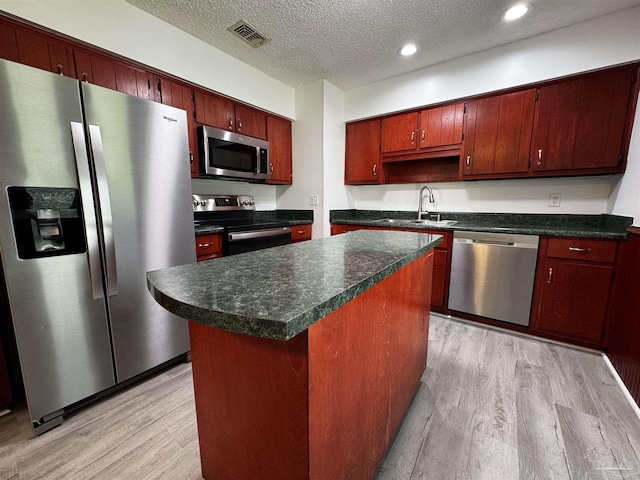 kitchen with visible vents, a sink, dark countertops, stainless steel appliances, and light wood finished floors