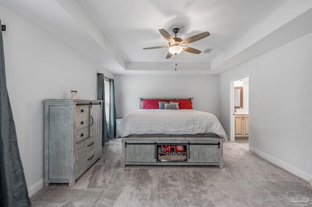 carpeted bedroom with ceiling fan, a raised ceiling, and ensuite bathroom