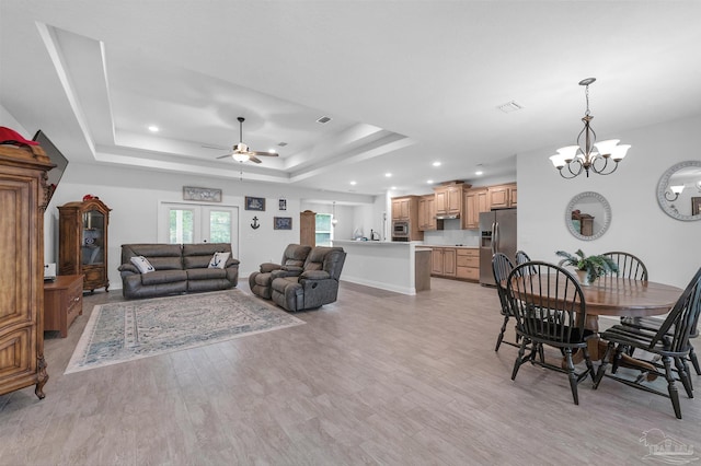 living room featuring a tray ceiling, light hardwood / wood-style floors, and ceiling fan with notable chandelier