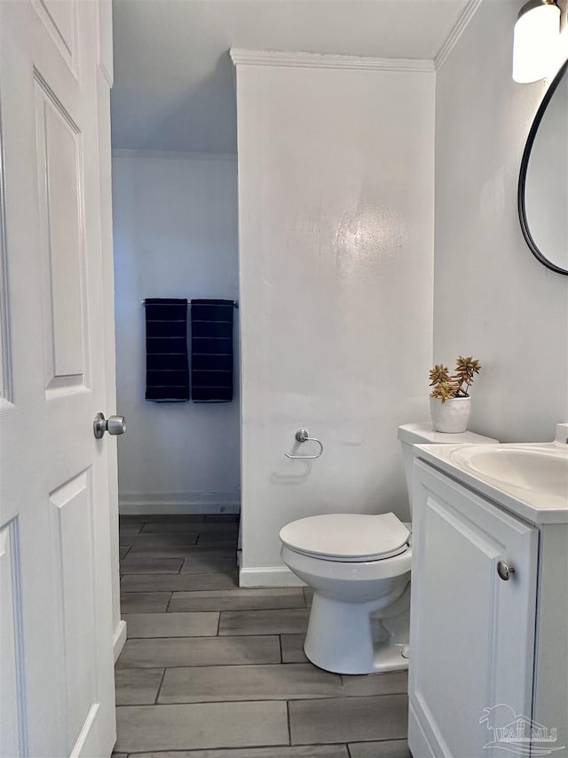 half bath featuring toilet, vanity, baseboards, ornamental molding, and wood tiled floor