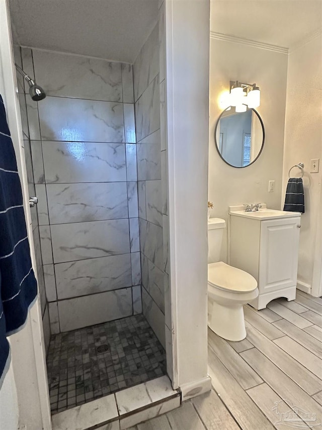 bathroom featuring crown molding, toilet, a tile shower, vanity, and baseboards