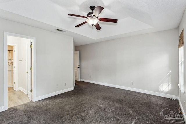 unfurnished bedroom with ceiling fan, a tray ceiling, ensuite bath, and carpet