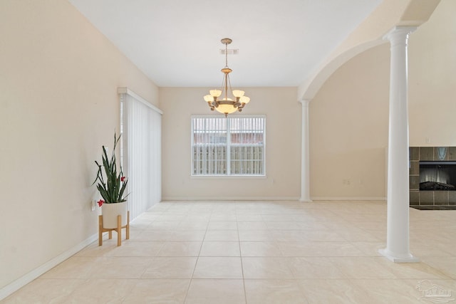 unfurnished dining area featuring a fireplace, a chandelier, light tile patterned floors, and ornate columns