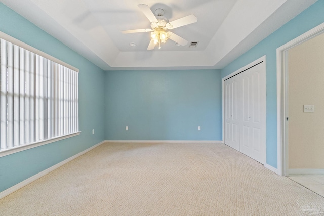 unfurnished bedroom with ceiling fan, light colored carpet, a closet, and a raised ceiling