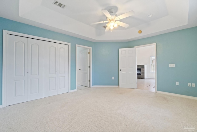 unfurnished bedroom featuring a tiled fireplace, light colored carpet, ceiling fan, a raised ceiling, and a closet