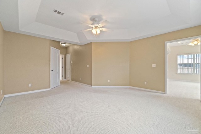 spare room with ceiling fan, a tray ceiling, and light carpet