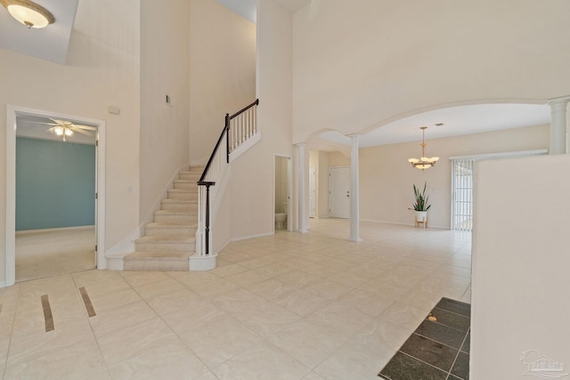 tiled foyer entrance with decorative columns, a towering ceiling, and ceiling fan with notable chandelier