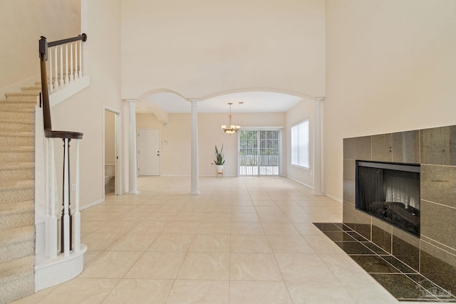 unfurnished living room featuring a fireplace, decorative columns, a high ceiling, light tile patterned floors, and a notable chandelier