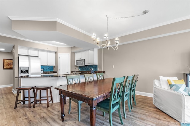 dining space featuring light wood finished floors, a notable chandelier, crown molding, and baseboards