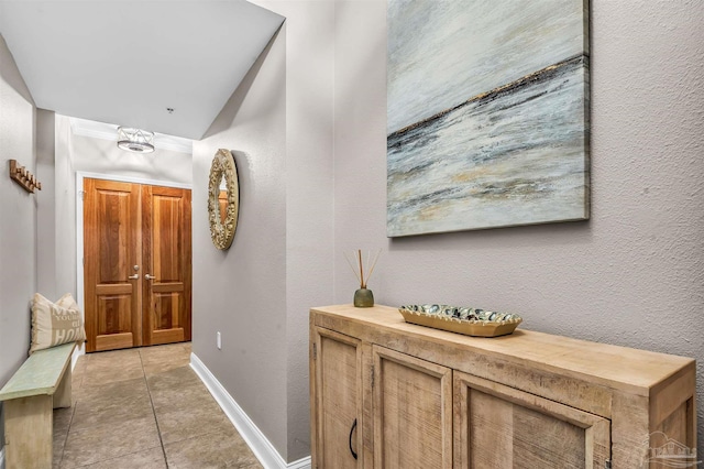 corridor with light tile patterned flooring, a textured wall, and baseboards