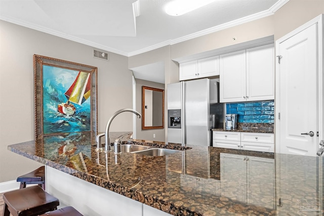 kitchen with visible vents, stainless steel refrigerator with ice dispenser, a sink, dark stone countertops, and crown molding