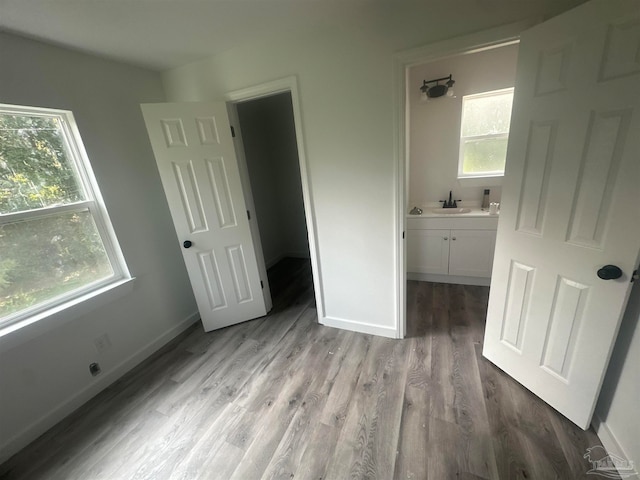 unfurnished bedroom with light hardwood / wood-style floors, a spacious closet, ensuite bathroom, and multiple windows