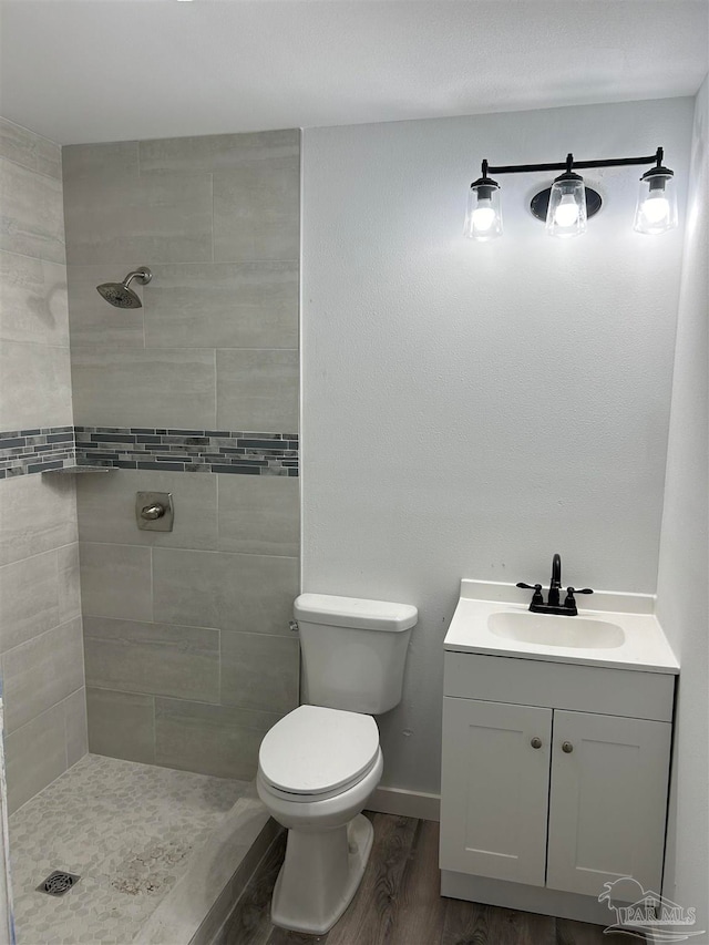 bathroom featuring toilet, hardwood / wood-style floors, vanity, and tiled shower