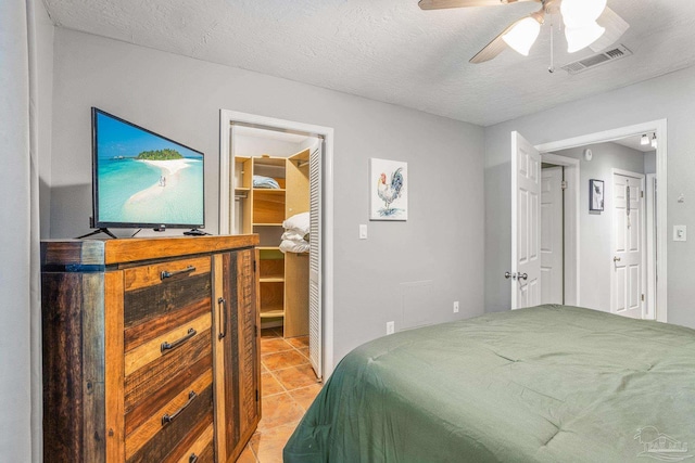 tiled bedroom with ceiling fan, a textured ceiling, and a walk in closet