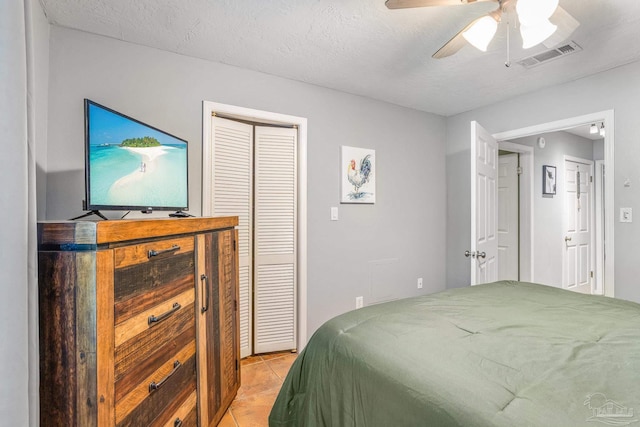 bedroom featuring ceiling fan, a closet, a textured ceiling, and light tile patterned floors