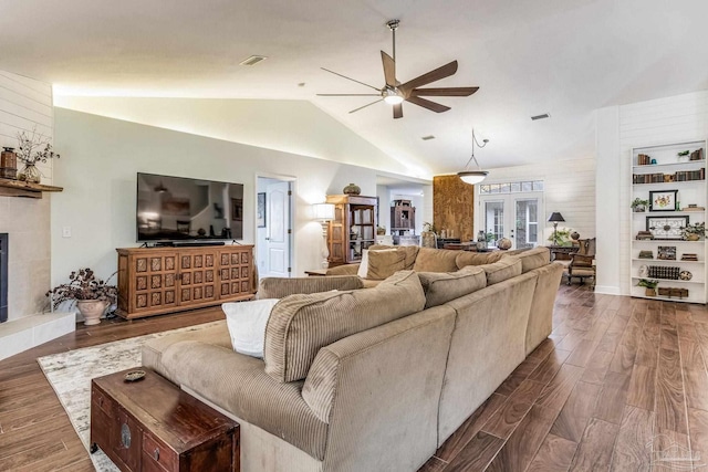 living room featuring ceiling fan, dark hardwood / wood-style flooring, a tiled fireplace, and vaulted ceiling