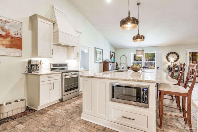 kitchen with hanging light fixtures, appliances with stainless steel finishes, a kitchen island with sink, and light stone counters