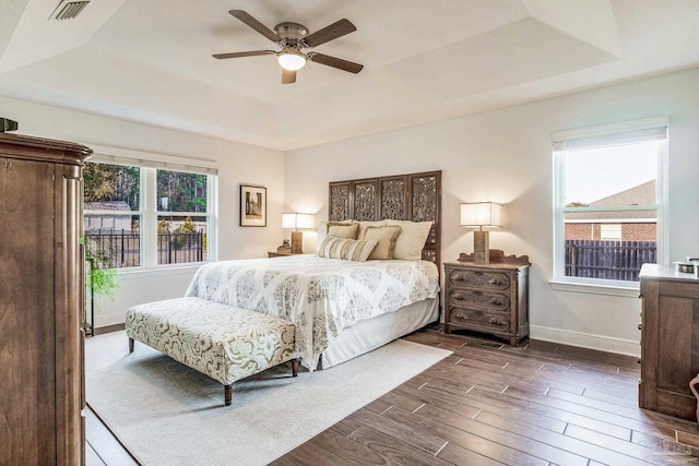 bedroom with multiple windows, dark hardwood / wood-style floors, ceiling fan, and a tray ceiling