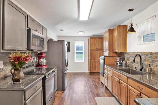 kitchen with decorative light fixtures, sink, dark stone countertops, stainless steel appliances, and dark wood-type flooring