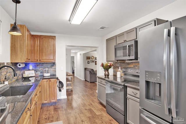 kitchen featuring sink, stainless steel appliances, tasteful backsplash, dark stone counters, and light wood-type flooring