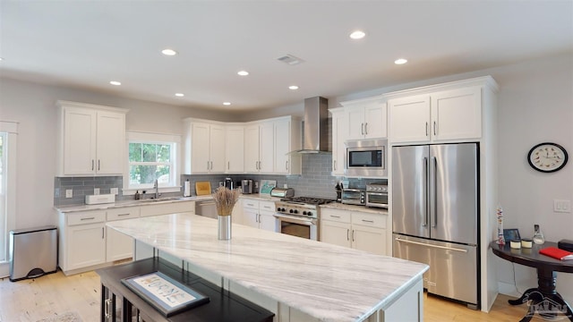 kitchen featuring wall chimney exhaust hood, white cabinets, and appliances with stainless steel finishes