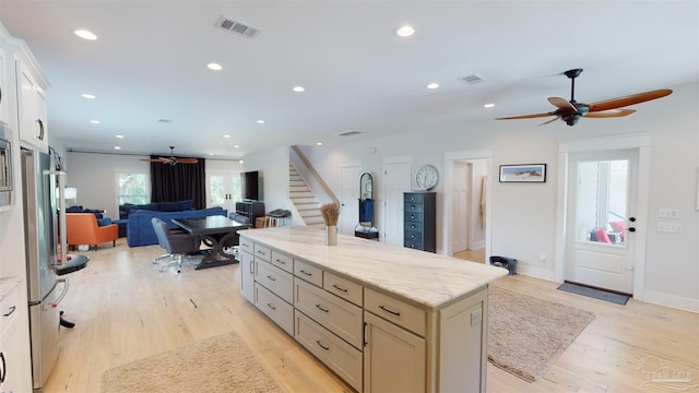 kitchen featuring light hardwood / wood-style floors, light stone counters, stainless steel refrigerator, a kitchen island, and ceiling fan