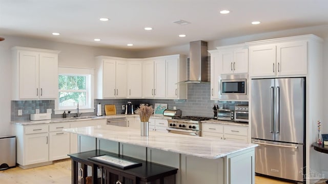 kitchen with wall chimney exhaust hood, white cabinetry, a center island with sink, and high quality appliances