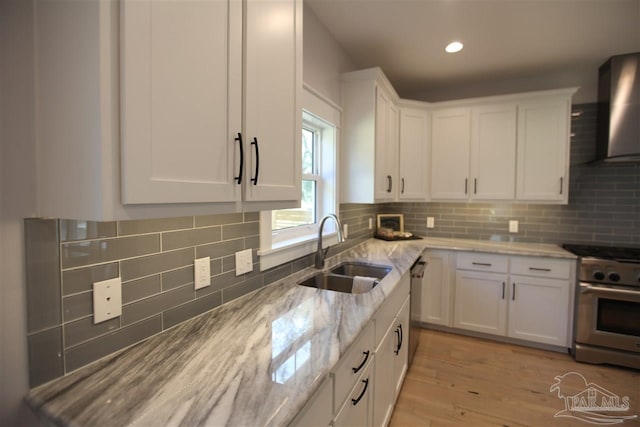 kitchen with appliances with stainless steel finishes, white cabinetry, light hardwood / wood-style flooring, sink, and wall chimney range hood