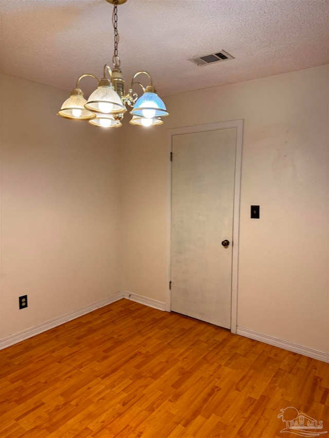 unfurnished room featuring a textured ceiling, an inviting chandelier, and light hardwood / wood-style flooring