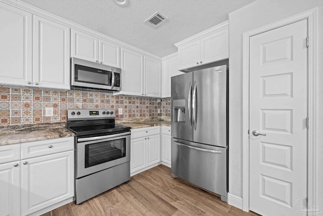 kitchen featuring white cabinets, light hardwood / wood-style flooring, decorative backsplash, stone countertops, and stainless steel appliances