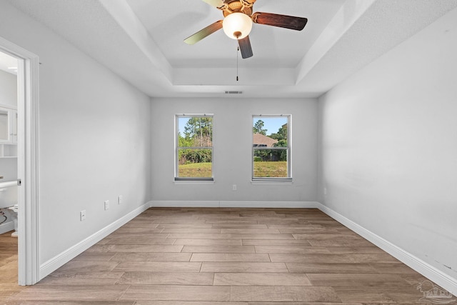 spare room with a raised ceiling, light hardwood / wood-style flooring, and ceiling fan